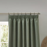 Dawn Reversible Pencil Pleat Curtains in eucalyptus green, showing pleated header hung on a chrome curtain pole with rings against a grey wall.