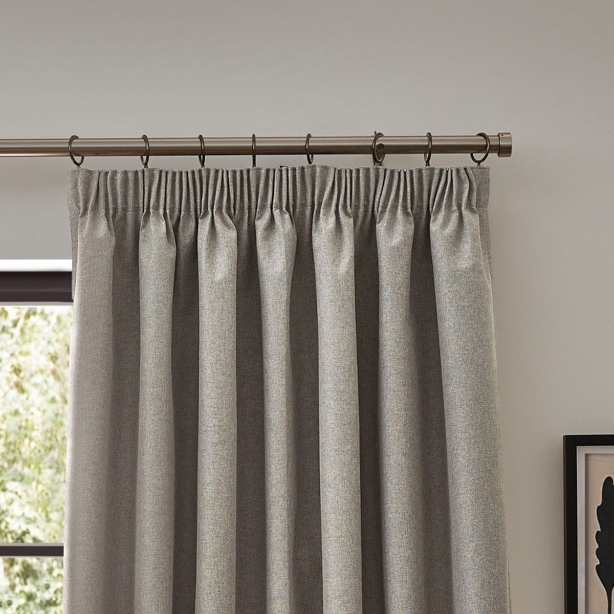 Dawn pencil pleat curtains in linen, showing pinch-pleated heading on a metal pole above a window in a neutral-toned room.