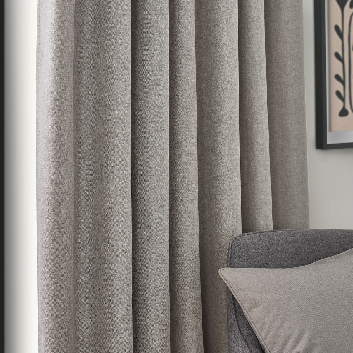 Dawn pencil pleat curtains in linen, shown in soft folds beside a grey armchair, with a woven marl-effect fabric in a muted beige tone.