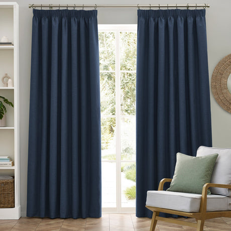 Dawn Plain Polyester Pencil Pleat Curtains in midnight blue, shown as a pair with tape-gathered heading, hung on a pole beside a window in a living room setting.