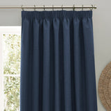 Dawn Plain Polyester Pencil Pleat Curtains in midnight blue, gathered on tape heading with metal rings on a pole, shown against a light grey wall near a window.