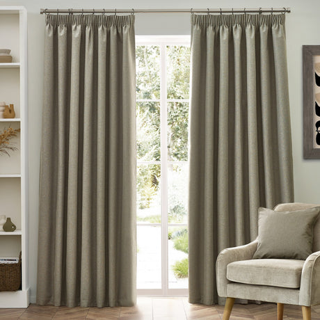 Dawn pencil pleat curtains in natural oatmeal marl-effect polyester, hung either side of a window in a living room with an armchair nearby.