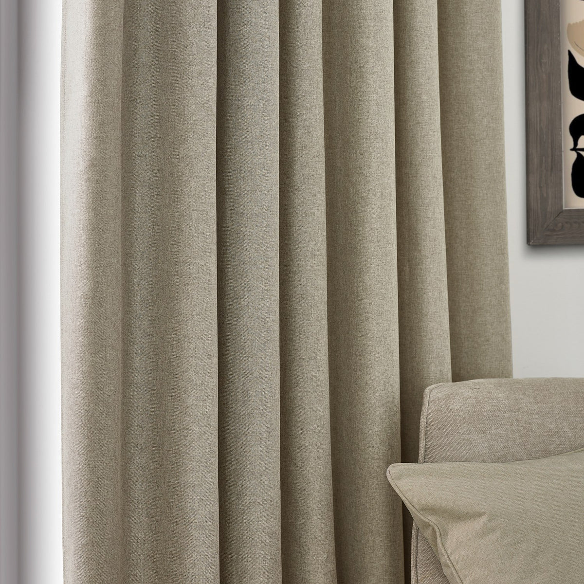 Dawn pencil pleat curtains in natural marl-effect polyester, shown floor-length in soft folds beside a window, with a beige sofa and framed art in the room.