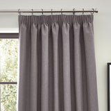 Dawn pencil pleat curtains in charcoal grey polyester with gathered heading tape, hung on curtain rings beside a window in a living room setting.