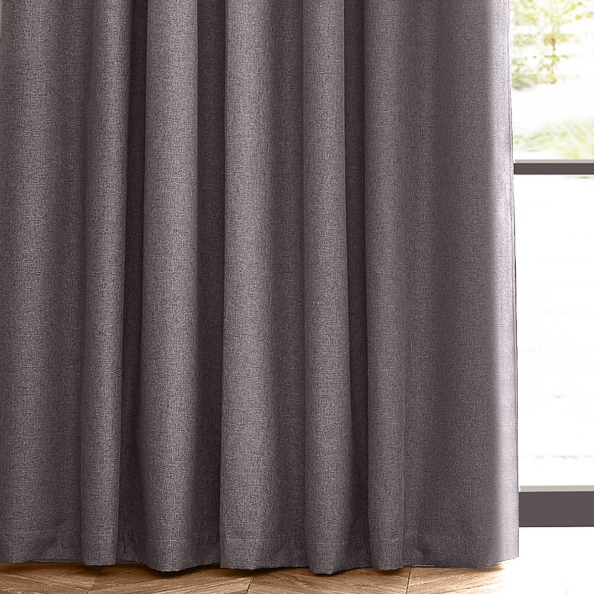 Dawn pencil pleat curtains in charcoal grey, close-up of pleated polyester fabric with a marl-effect texture, hung by a window with wooden flooring.