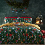 Deck The Halls polycotton duvet cover set in pine green, printed with baubles, poinsettias, animals and foliage, styled on a bed with matching pillowcases and a red cushion trim.