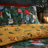 Deck The Halls polycotton duvet cover set showing pine green side with baubles, candle, cherub and poinsettia print, reverse in mustard-gold with holly and berry sprigs.