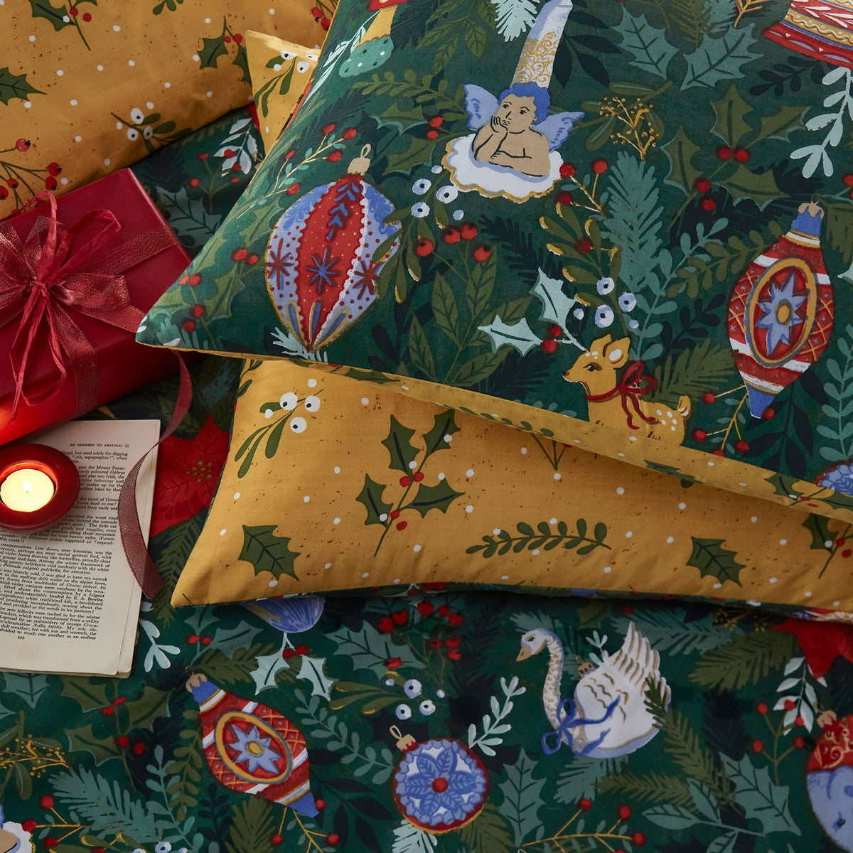 Deck The Halls polycotton duvet cover set in pine green, printed with baubles, holly, a cherub, deer and swan, paired with a mustard-gold reverse pillowcase.