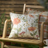 Delamere Reversible Linen Cushion in Russet, showing a cream floral wildflower side, with a check-pattern cushion behind on a wooden garden bench.