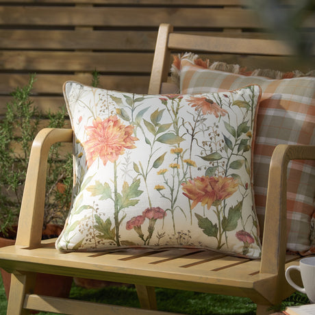 Delamere Reversible Linen Cushion in Russet, showing a cream floral wildflower side, with a check-pattern cushion behind on a wooden garden bench.