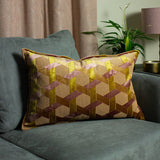 Delano Jacquard Velvet Cushion in ochre, olive and blush pink, geometric lattice pattern, shown on a teal sofa in a living room.