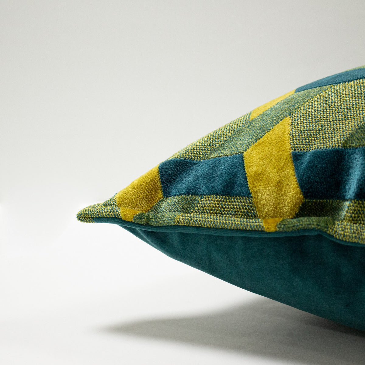 Delano Jacquard Velvet Cushion in teal and gold, close-up of the bolster corner showing an interlocking lattice pattern with raised velvet pile against woven cloth, set on a plain light background.
