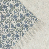 Delphine Floral Cotton Throw in Delph Blue, showing a cream cotton weave printed with dusty blue and green flowers, edged with knotted fringe.