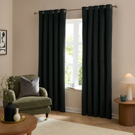 Black velvet eyelet curtains with metal ring headers hung on a chrome pole, shown floor-length either side of a window in a living room with a green armchair.
