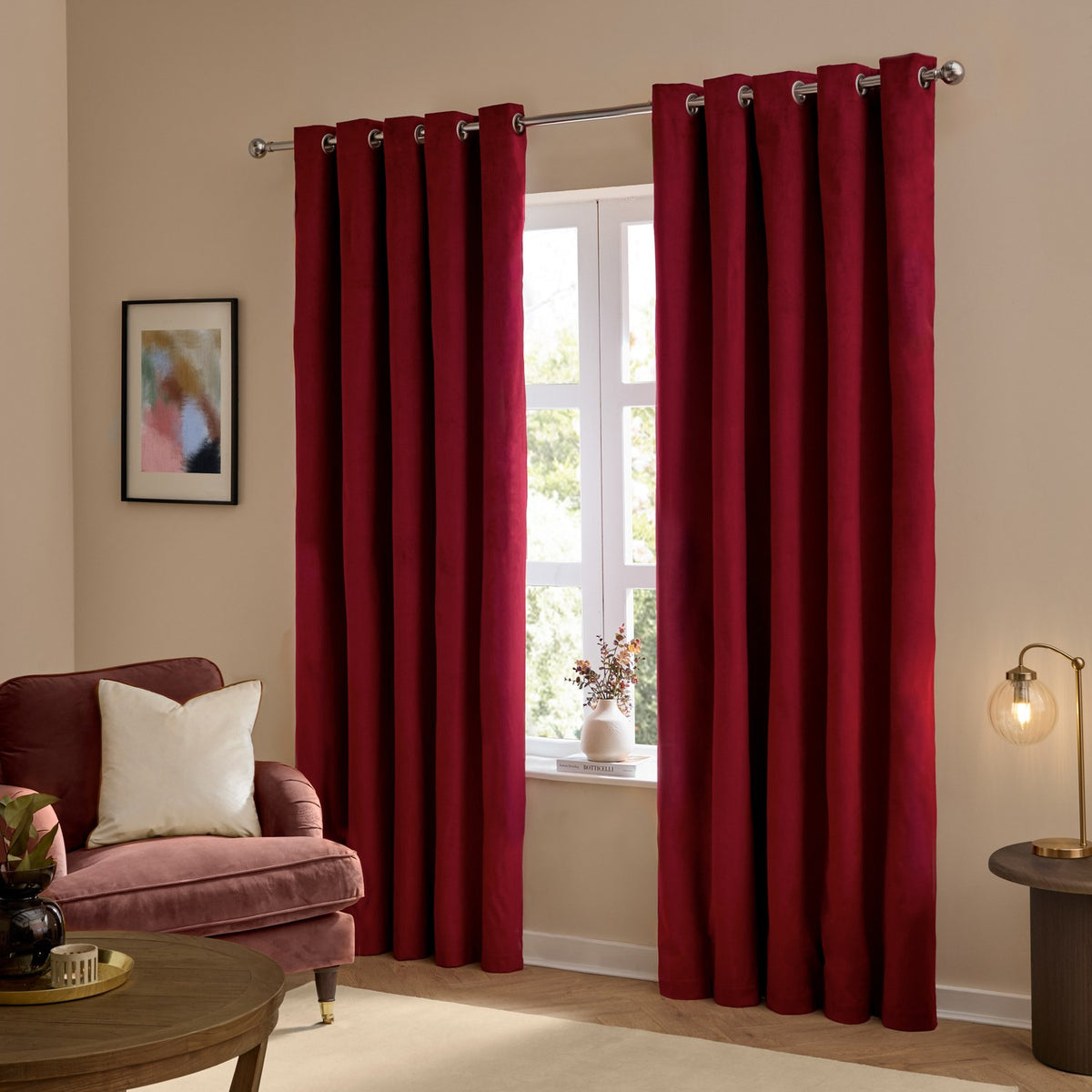 Burgundy velvet eyelet curtains hanging in a living room, shown as a pair framing a window, with silver eyelet rings on a chrome pole above.