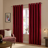 Burgundy velvet eyelet curtains hanging in a living room, shown as a pair framing a window, with silver eyelet rings on a chrome pole above.