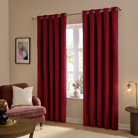 Burgundy velvet eyelet curtains hanging in a living room, shown as a pair framing a window, with silver eyelet rings on a chrome pole above.
