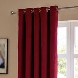 Burgundy velvet eyelet curtain with silver grommets hung on a chrome pole beside a white-framed window in a living room setting.