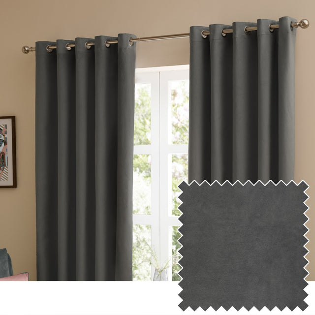 Charcoal grey velvet eyelet curtains with matt finish hung on a metal pole in a living room window, shown with a fabric swatch of the same colour.
