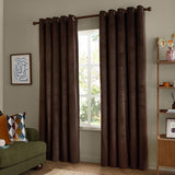 Chocolate brown velvet eyelet curtains with grommet header hung on a wooden pole, shown fully lined in a living room beside a window.