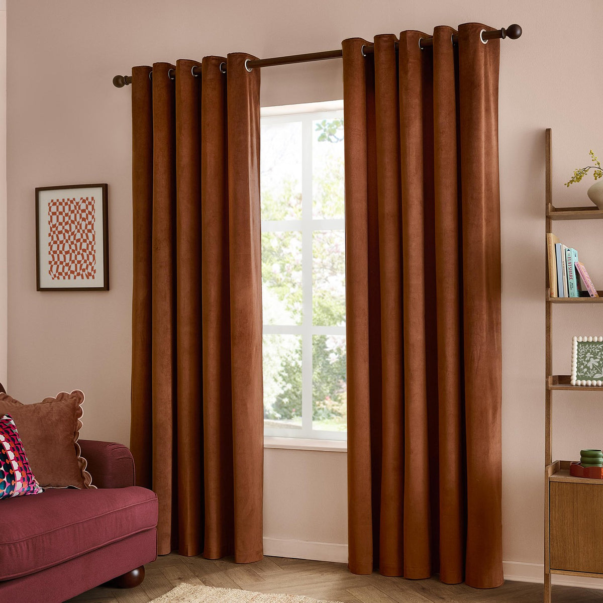 Rust-brown velvet eyelet curtains with metal grommets on a dark pole, shown fully drawn either side of a window in a living room setting.