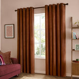 Rust-brown velvet eyelet curtains with metal grommets on a dark pole, shown fully drawn either side of a window in a living room setting.