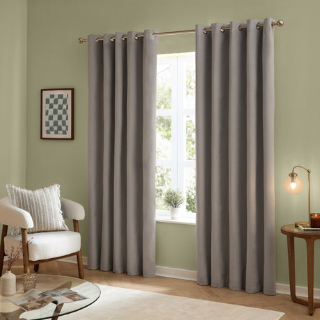 Silver-grey velvet eyelet curtains with metal grommet rings on a pole, shown floor-length either side of a window in a green-walled living room.