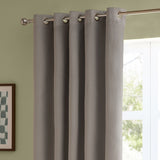 Silver-grey velvet eyelet curtains with metal grommets hung on a chrome pole, shown in a living room beside a green wall and window.
