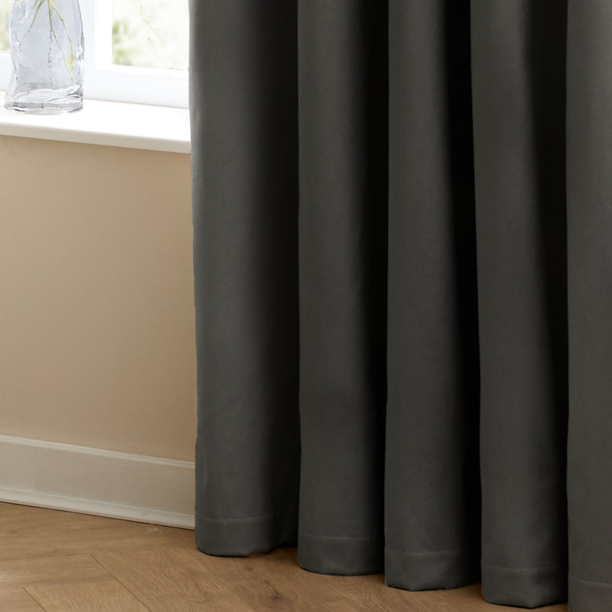 Charcoal velvet pencil pleat curtain in a room setting, showing soft folds falling to the floor beside a white-framed window and glass vase on the sill.