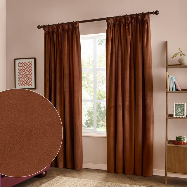 Rust-toned velvet pencil pleat curtains hanging from a dark pole in a bedroom, with a fabric swatch inset showing the textured polyester weave.
