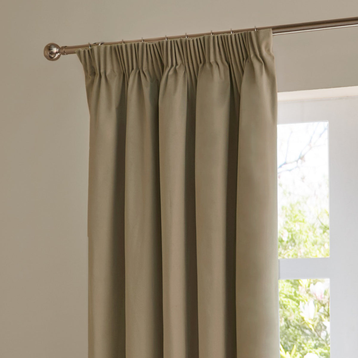 Mocha velvet pencil pleat curtains with pinch-pleated heading on a chrome pole, shown hanging beside a bright window in a room with light walls.