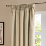 Natural beige velvet pencil pleat curtains hanging on a chrome pole beside a window, showing soft folds and gathered heading tape in a living room setting.