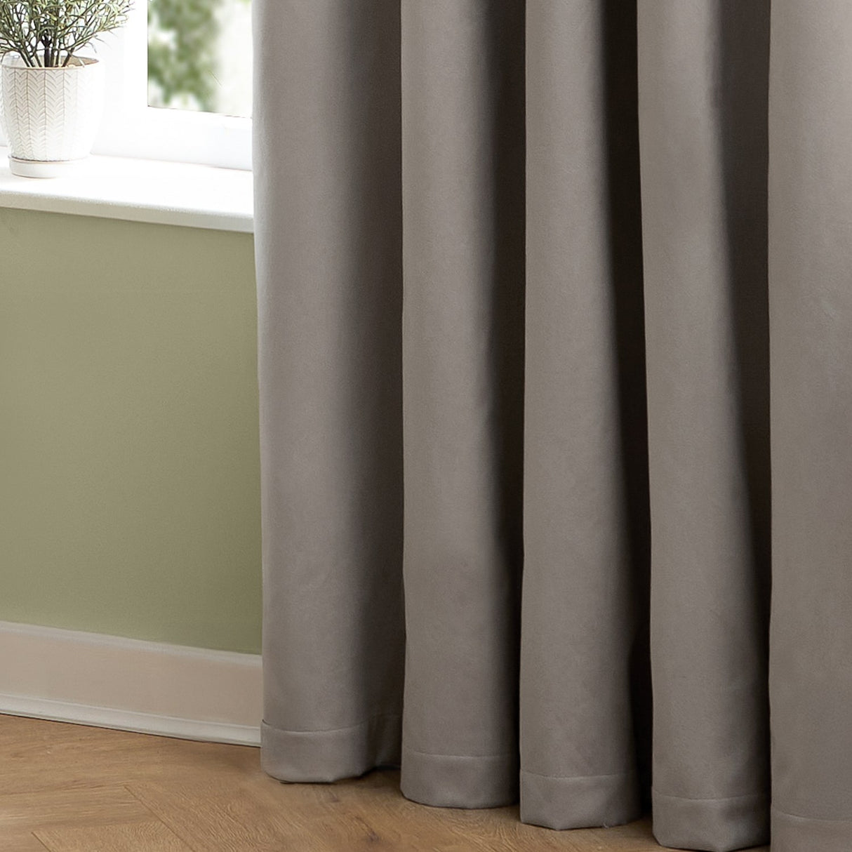 Silver-grey velvet pencil pleat curtains in soft matte polyester hanging in deep folds beside a window with green walls and wooden flooring.