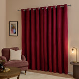 Burgundy velvet eyelet curtains with silver grommets hung on a chrome pole, shown floor-length in a living room beside an armchair and floor lamp.