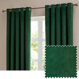 Emerald green velvet eyelet curtains hanging on a chrome rod by a window, shown with a fabric swatch sample of the same matt velvet material.