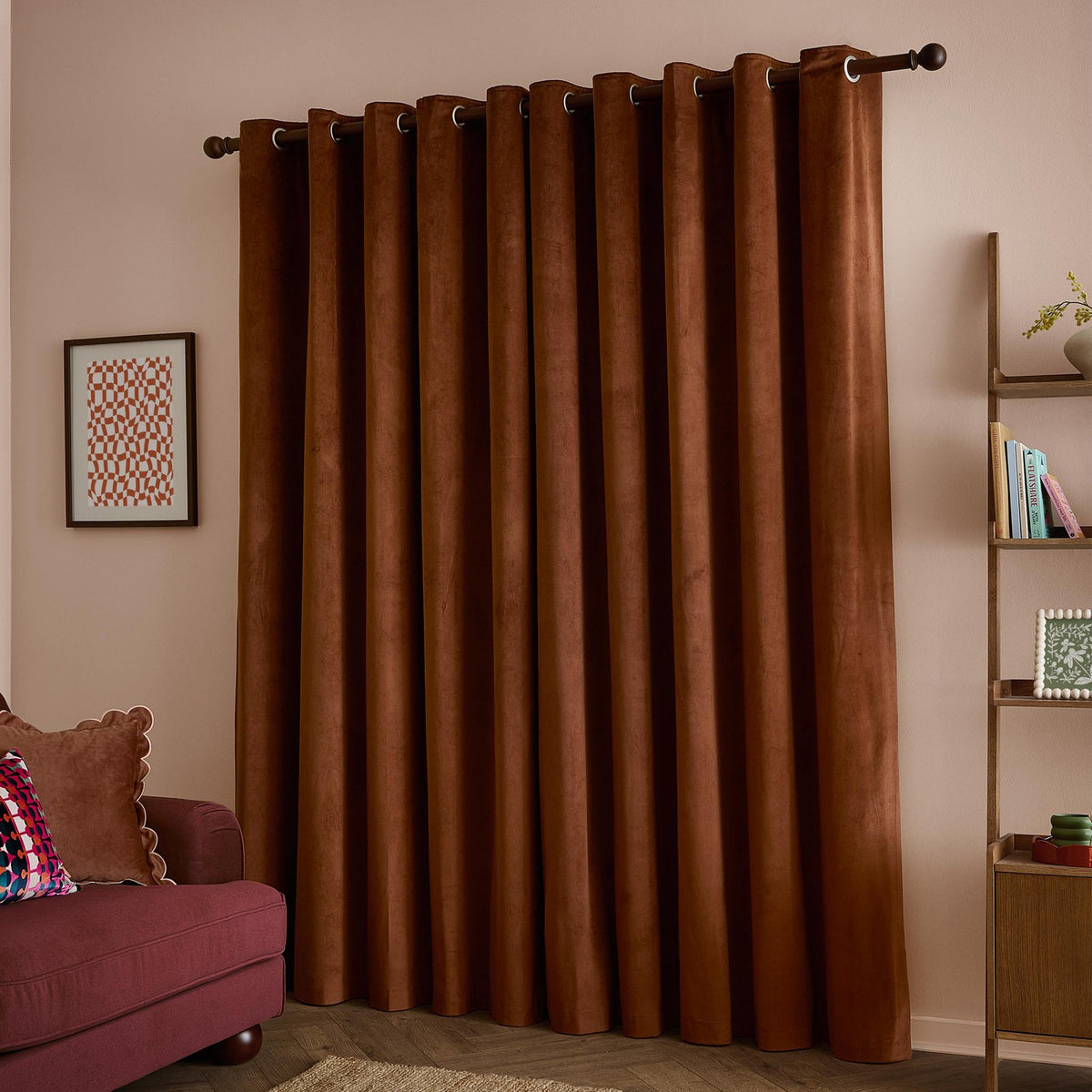Velvet eyelet curtains in mink brown hung on a dark pole in a living room, showing the soft pile texture and grommet header above a burgundy sofa.