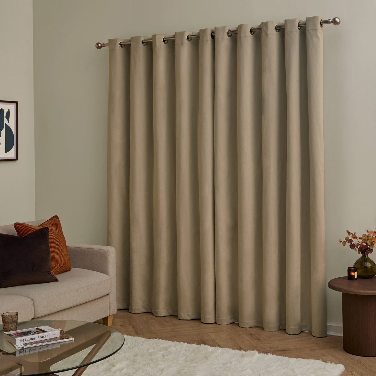Mocha velvet eyelet curtains with grommet header hung on a metal pole, shown floor-length in a living room beside a beige sofa and wooden side table.