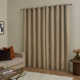 Mocha velvet eyelet curtains with grommet header hung on a metal pole, shown floor-length in a living room beside a beige sofa and wooden side table.