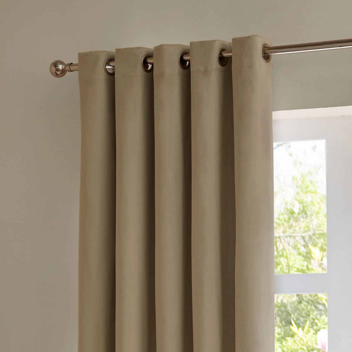 Mocha velvet eyelet curtains with metal grommets on a brushed rod, shown hanging beside a window in a plain-walled room.