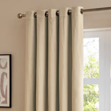 Natural velvet eyelet curtains hanging on a chrome rod beside a window, showing the matt fabric texture and metal grommet header in a living room setting.