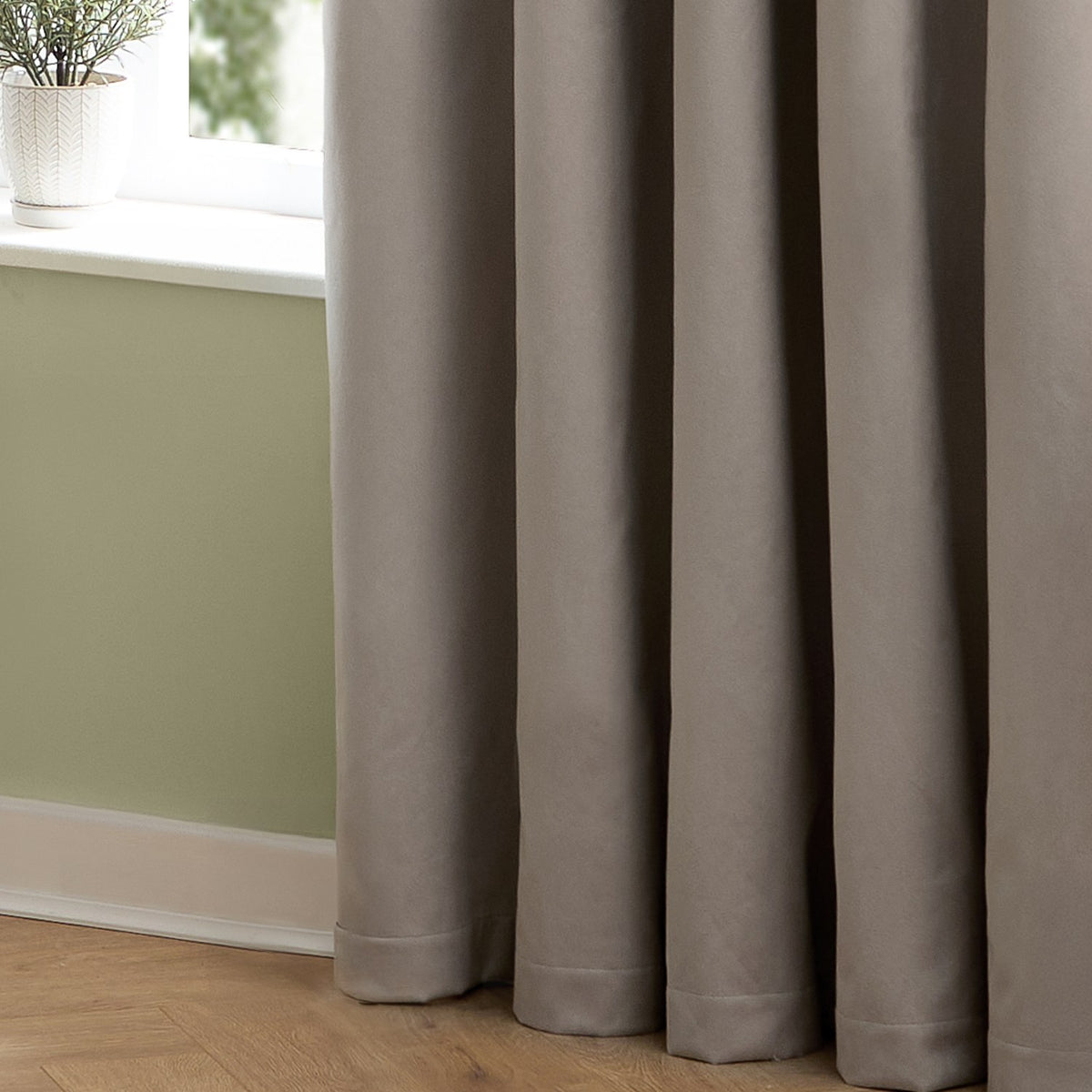 The Ultimate Velvet Plain Lined Eyelet Curtains in Silver, shown in soft matte velvet with deep folds and an eyelet header, styled beside a window in a living room with sage green walls.