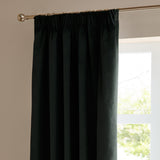 Black velvet pencil pleat curtain with gathered header hooked onto a metal pole, hanging beside a window in a living room setting.