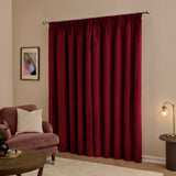 Burgundy velvet pencil pleat blackout curtains on a chrome pole, styled in a living room with a pink armchair, gold lamp and framed wall art.