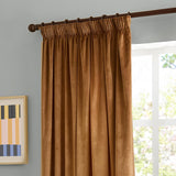 Caramel velvet pencil pleat curtain with pinch-pleated heading on a dark rod, shown hanging beside a window in a grey-walled living room.