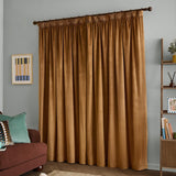 Caramel velvet pencil pleat curtains with pleated heading on a dark rod, shown floor-length in a living room beside a bookshelf and armchair.