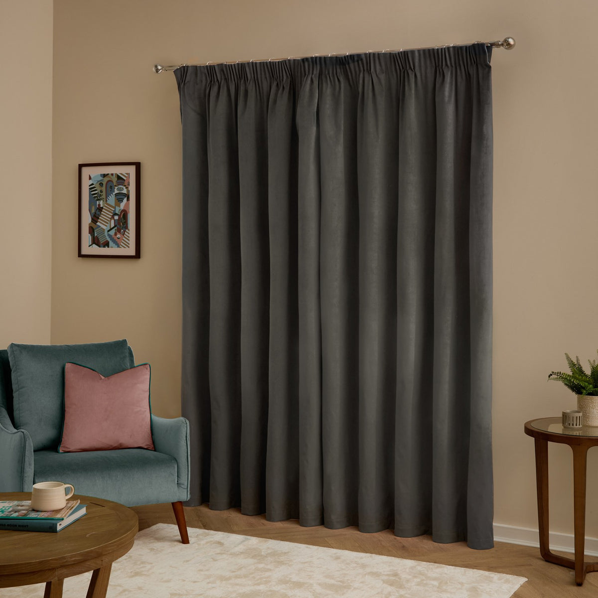 Charcoal velvet pencil pleat curtains hung on a metal pole in a living room, shown with a teal armchair, wood side tables, and framed wall art.