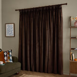 Chocolate brown velvet pencil pleat curtains with pinch-pleat heading on a dark rod, shown floor-length in a living room beside an armchair and shelving unit.