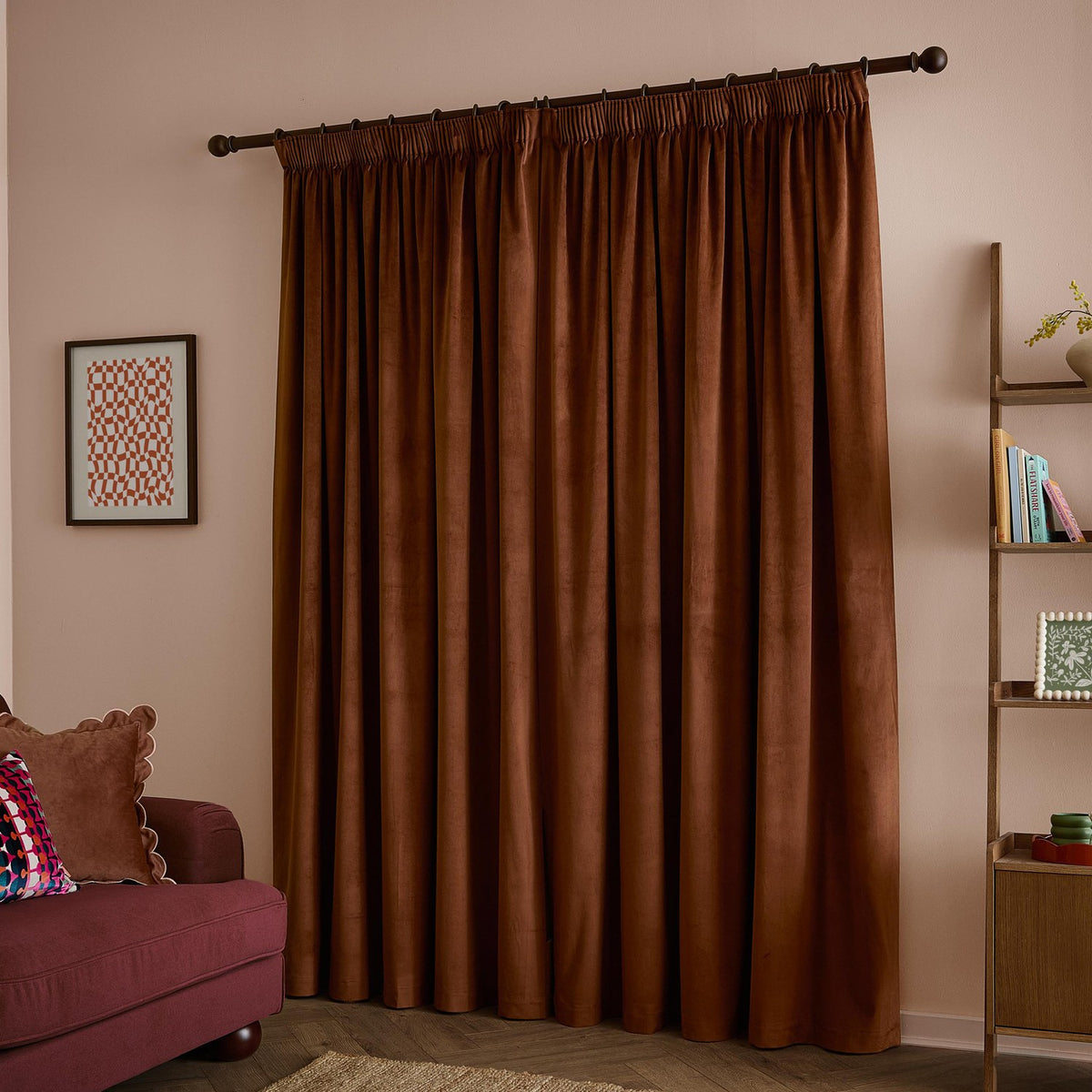 Rust-brown velvet pencil pleat curtains with a matt finish hanging fully drawn on a dark rod in a living room with pink walls.
