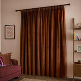 Rust-brown velvet pencil pleat curtains with a matt finish hanging fully drawn on a dark rod in a living room with pink walls.