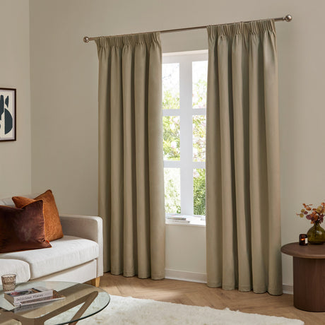 Mocha velvet pencil pleat curtains hung either side of a living room window, shown paired with a beige sofa and rust-toned cushions.